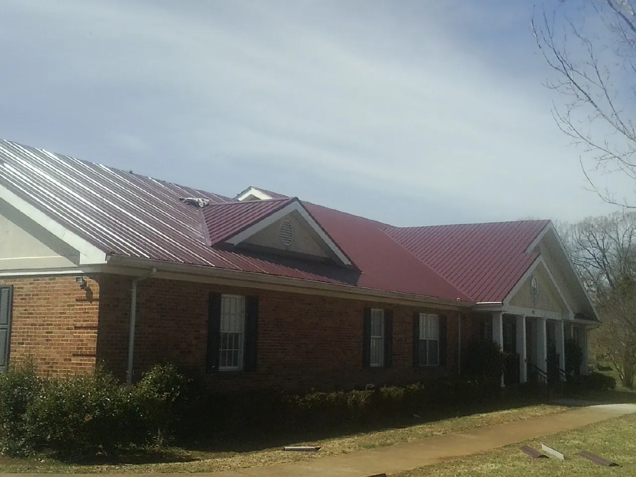Red metal roof with gabled entries on a long brick building, from a Hail Damage Roof Repair job in Fredonia